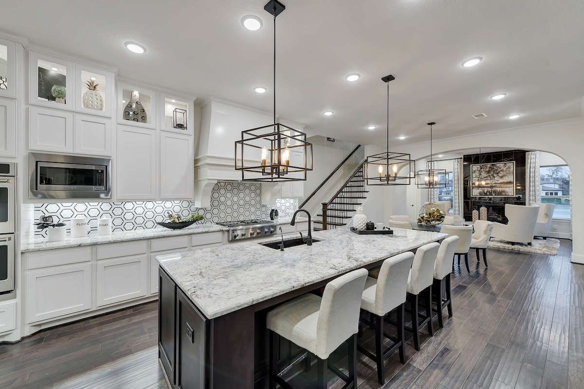 Modern kitchen with white cabinets, dark island with seating, pendant lights, and stainless steel appliances.