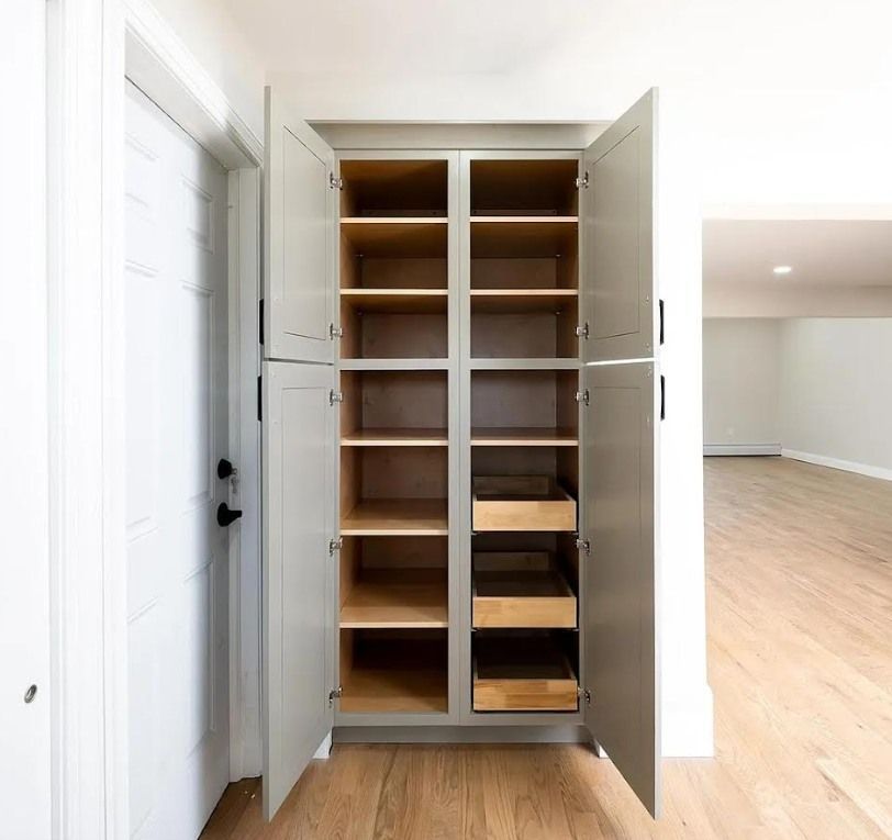 Empty pantry with gray doors and wooden shelves and drawers, near a door.