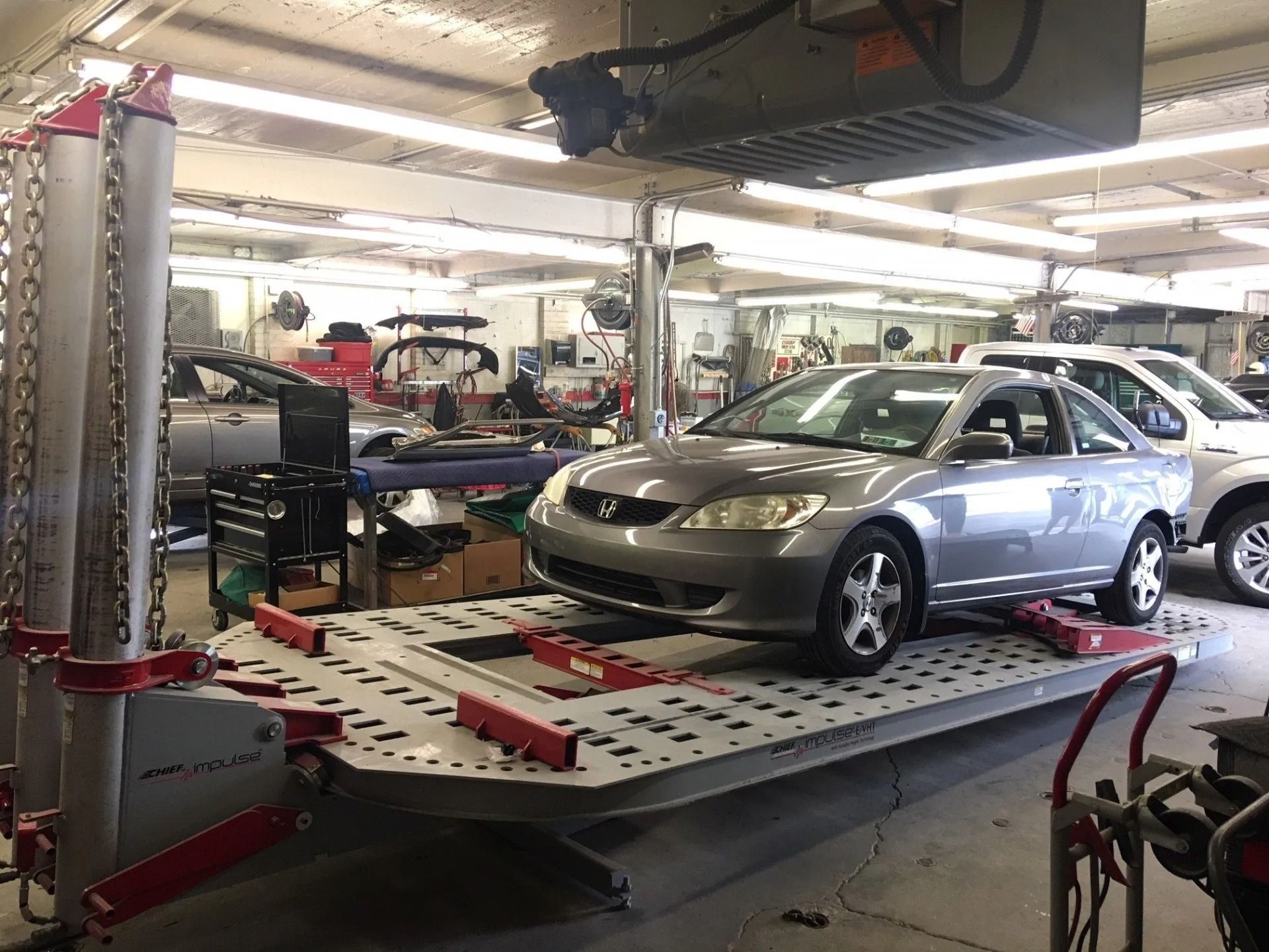 Silver car on a frame straightening machine in a repair shop.