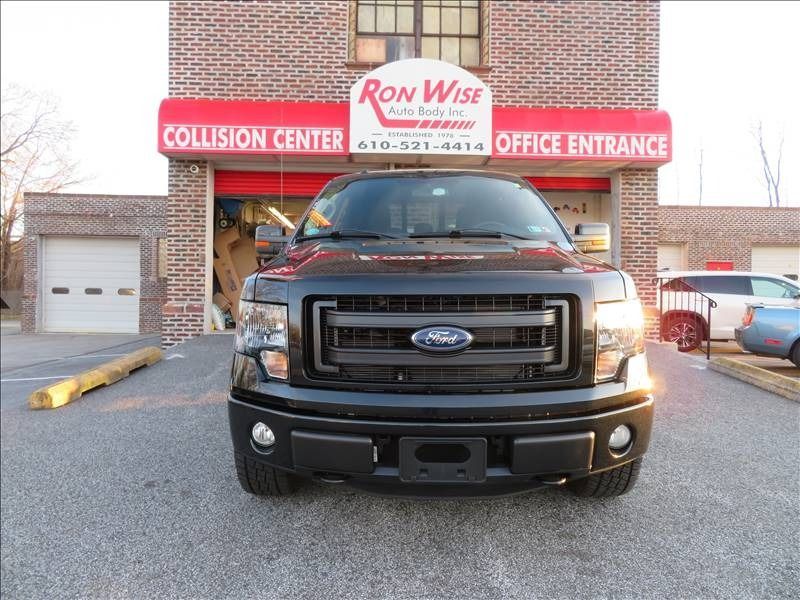 Black Ford F-150 truck parked in front of Ron Wise Collision Center with red awning.