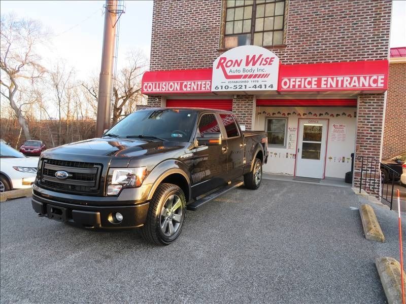 Black Ford F-150 truck parked in front of Ron Wise Auto Body, a collision center, office entrance.