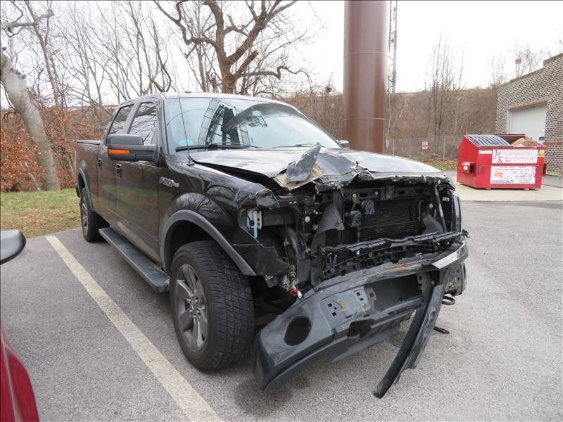 Damaged black pickup truck in a parking lot, front end heavily damaged.
