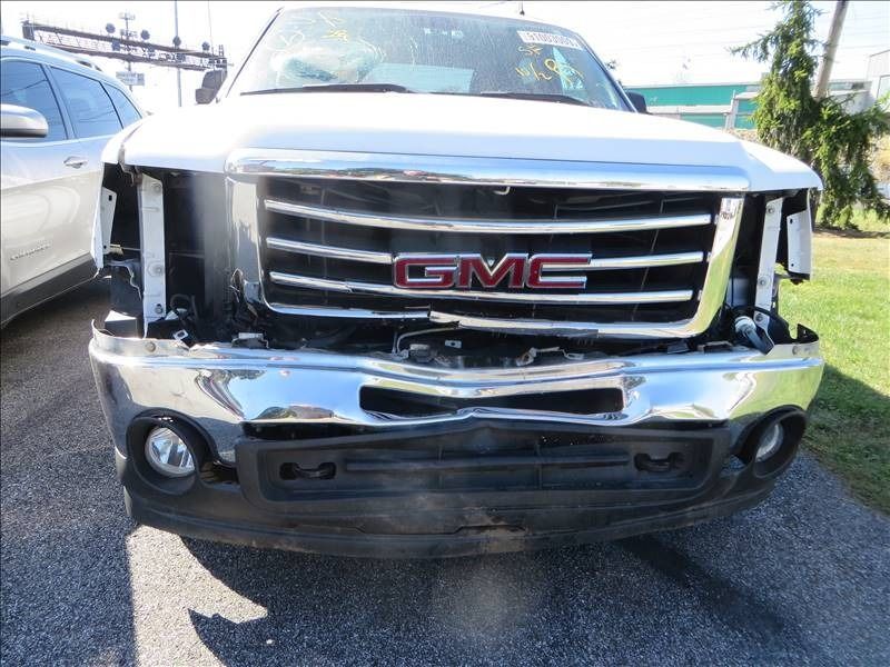 Damaged silver GMC truck with missing headlights and a dented bumper.