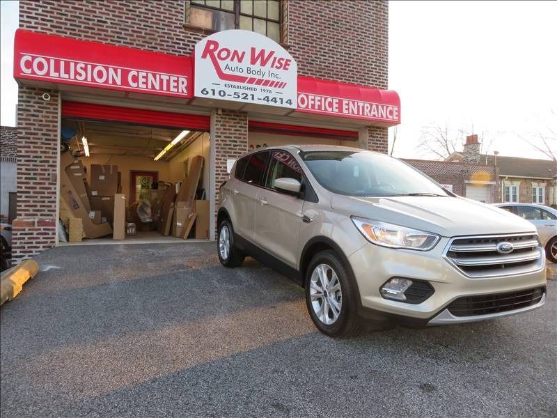 Tan Ford SUV parked in front of Ron Wise Collision Center with open shop entrance.