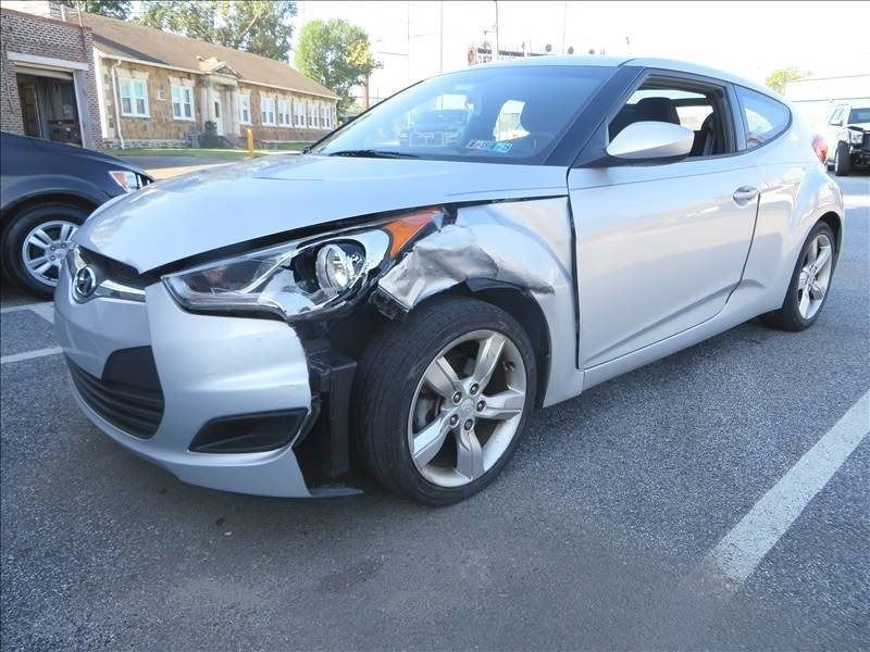 Silver Hyundai Veloster with front-end damage parked in a lot.