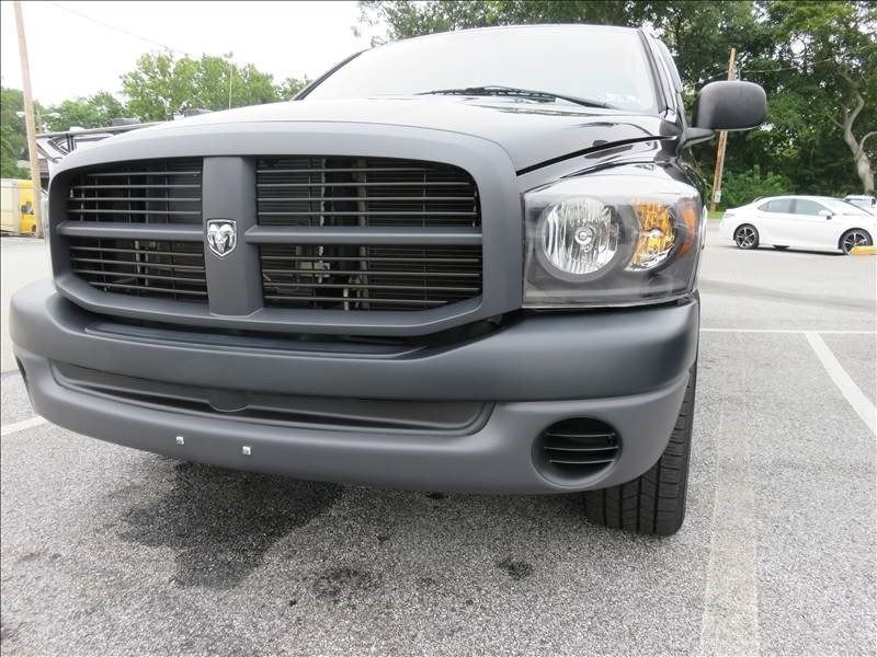 Black Dodge Ram truck parked in a lot, with a white car in the background.