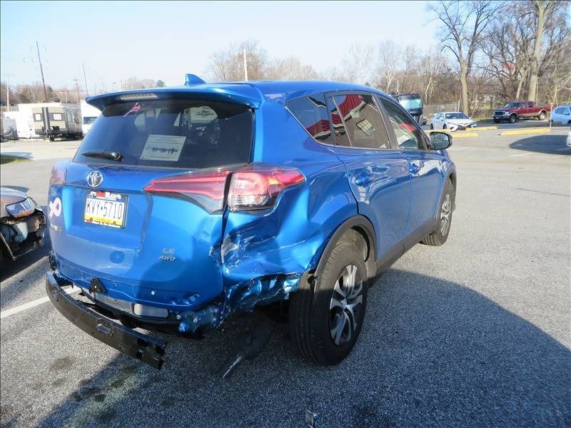 Blue Toyota RAV4 with rear-end damage, parked in a lot on a sunny day.
