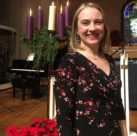 Woman in floral dress smiles by Advent wreath in church. Piano in background.