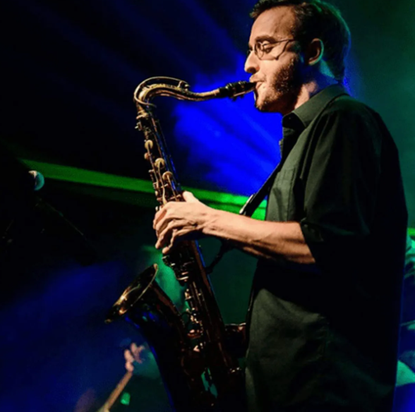 Man playing saxophone on stage under blue and green lights.