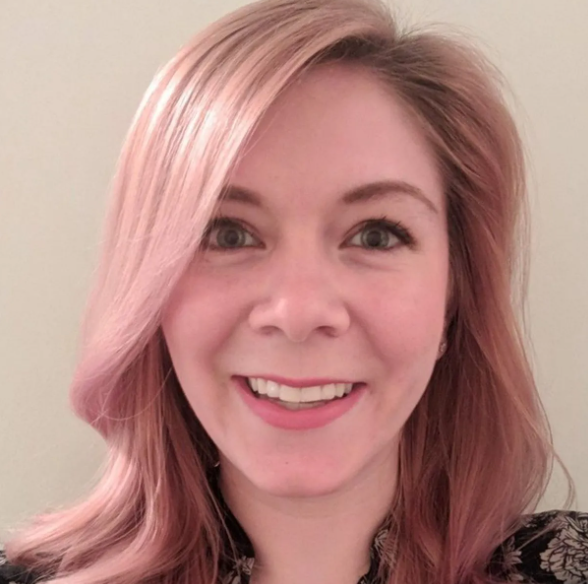 Woman with pink hair smiles, looking at the camera.