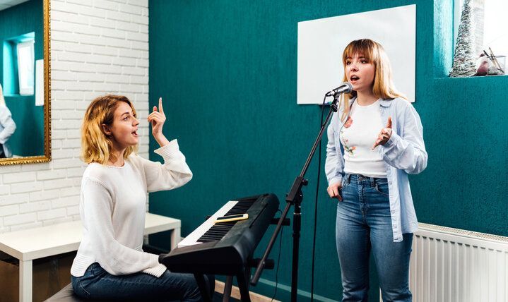 Two people in a music studio, one playing an electronic keyboard while the other sings into a microphone.