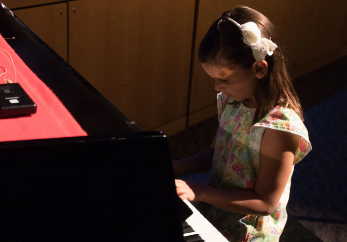 Young person playing piano with focus; white flower hair clip.