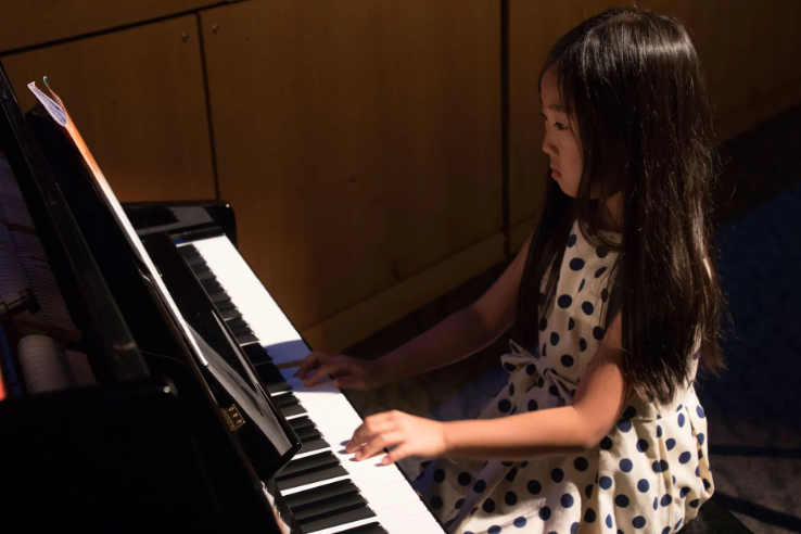 Young girl playing a piano, wearing a polka dot dress.