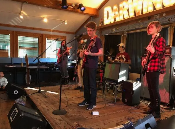 Band performing on a stage. Musicians play guitars, drums, in a venue with 