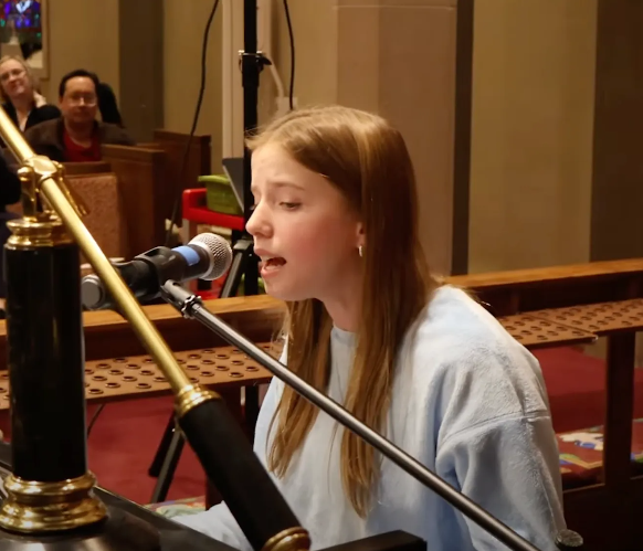 Girl singing into a microphone inside a building.
