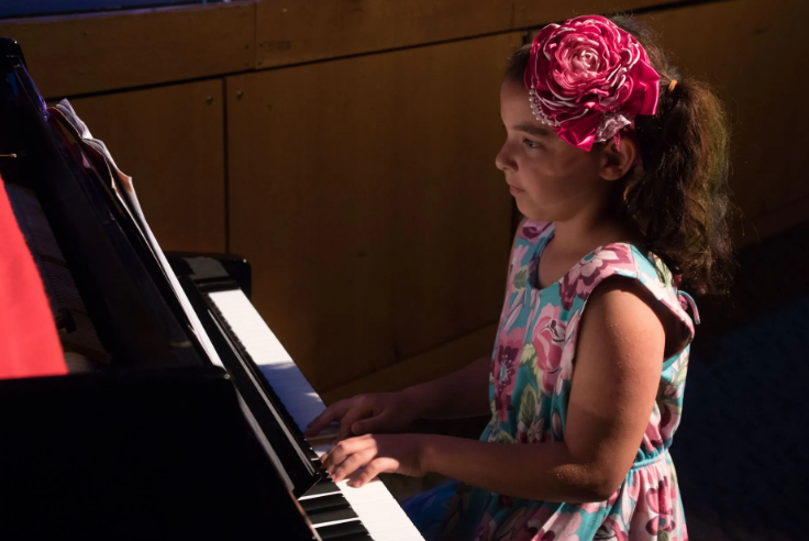 Girl with pink flower in hair plays piano.