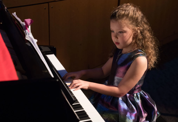 Young person in a sparkly dress playing a piano, focused expression.