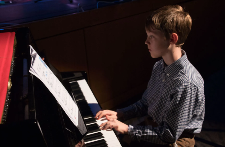 Young person playing piano, looking at sheet music. Indoors, dim lighting.