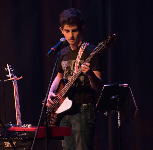 Man playing bass guitar on stage with microphone and sheet music.