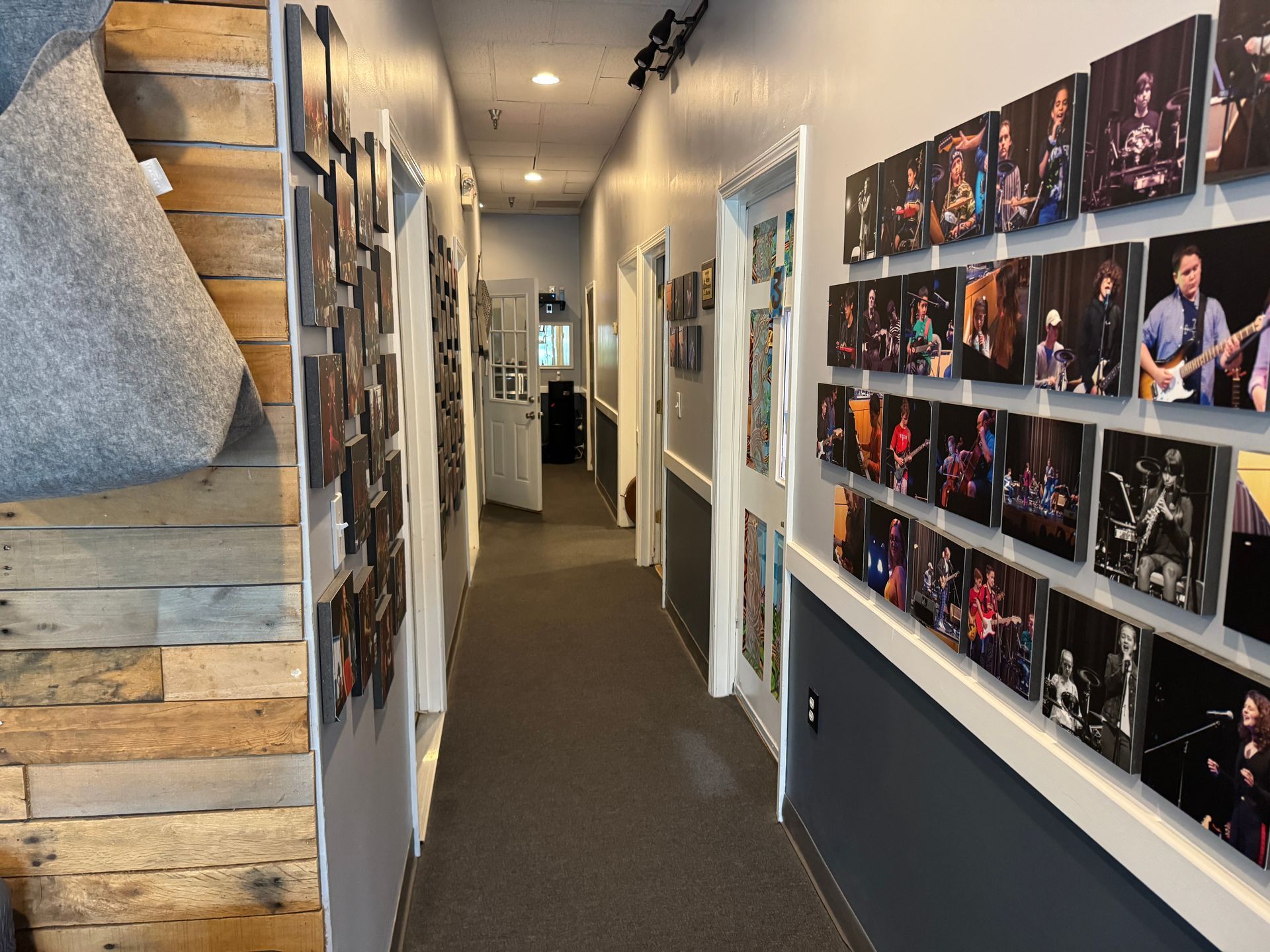 Narrow hallway with doors and framed photos on walls. Carpeted floor, white trim, and a pallet-style wall.