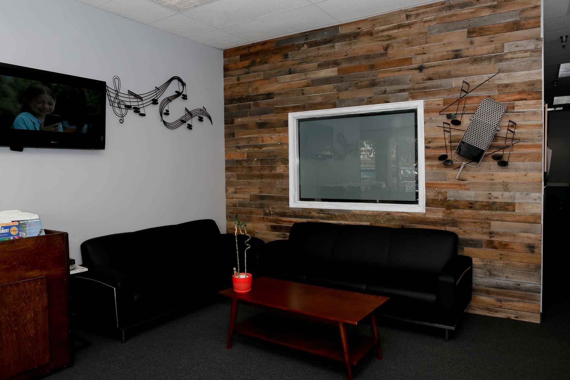Waiting room with black couches, a wood-paneled wall, and a TV.