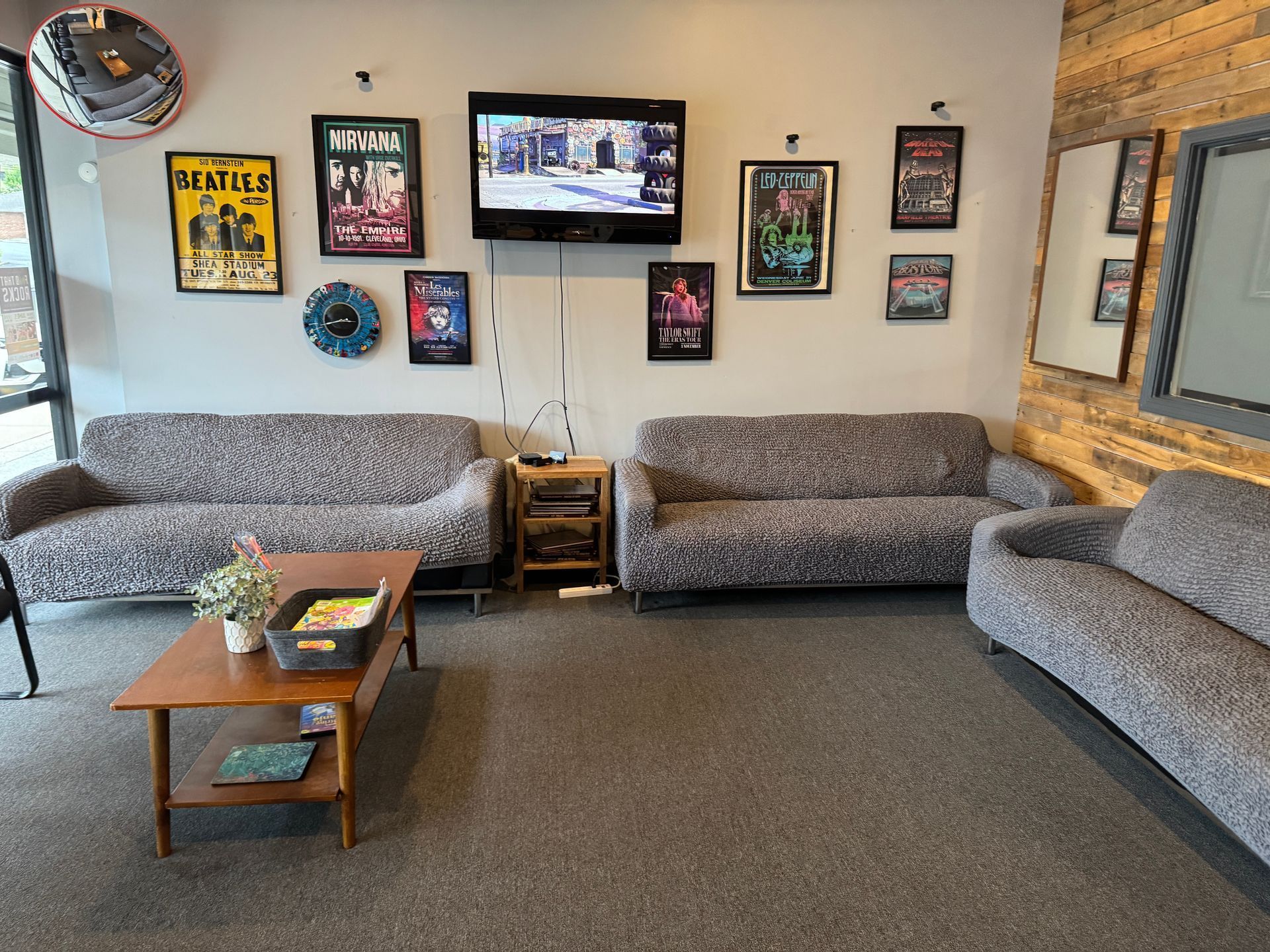 Lounge area with gray sofas, a coffee table, and framed movie posters on a wall. A TV is mounted above the center sofa.