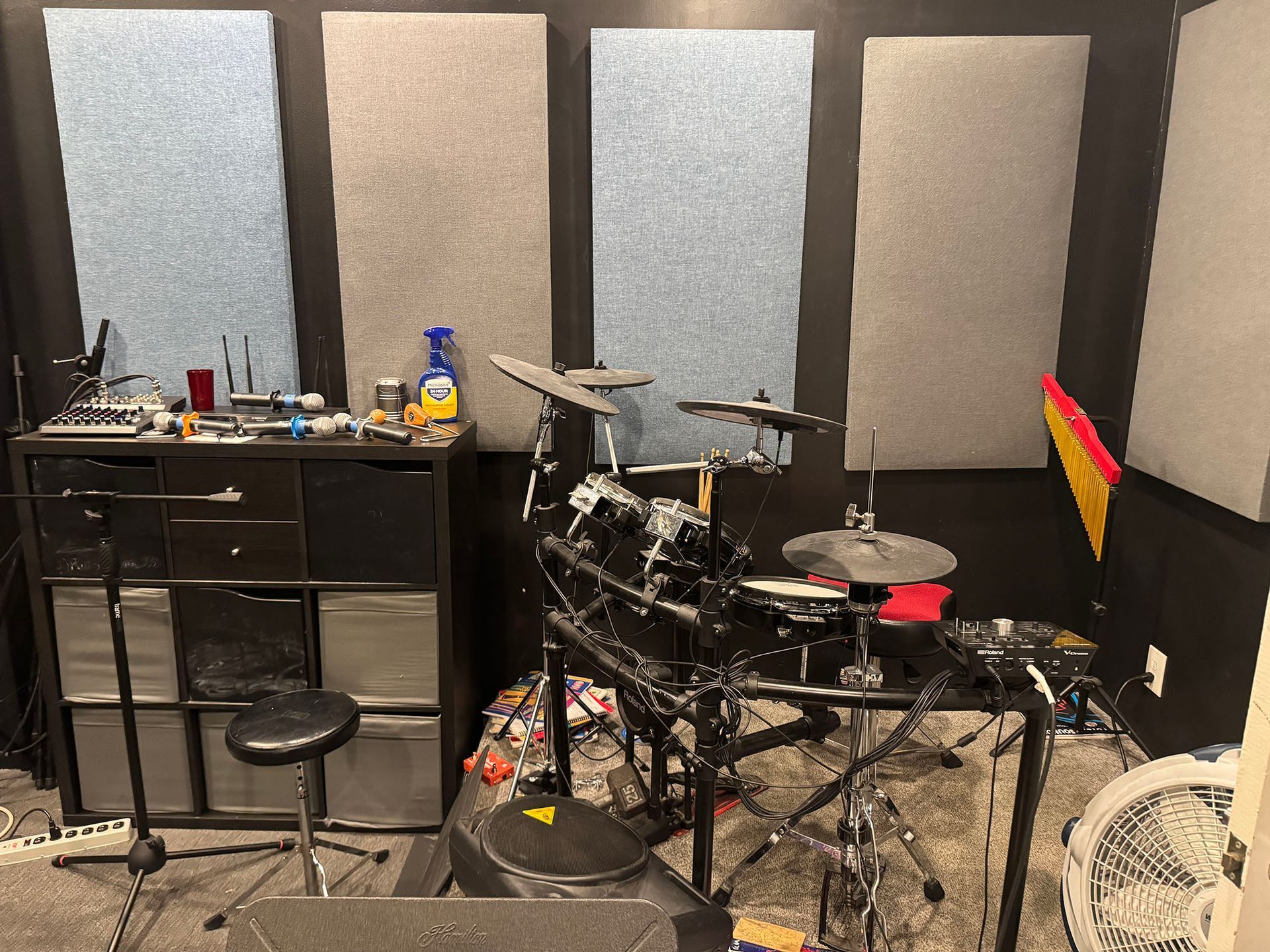 Acoustic panels in a music room with an electronic drum kit, storage, and a fan.