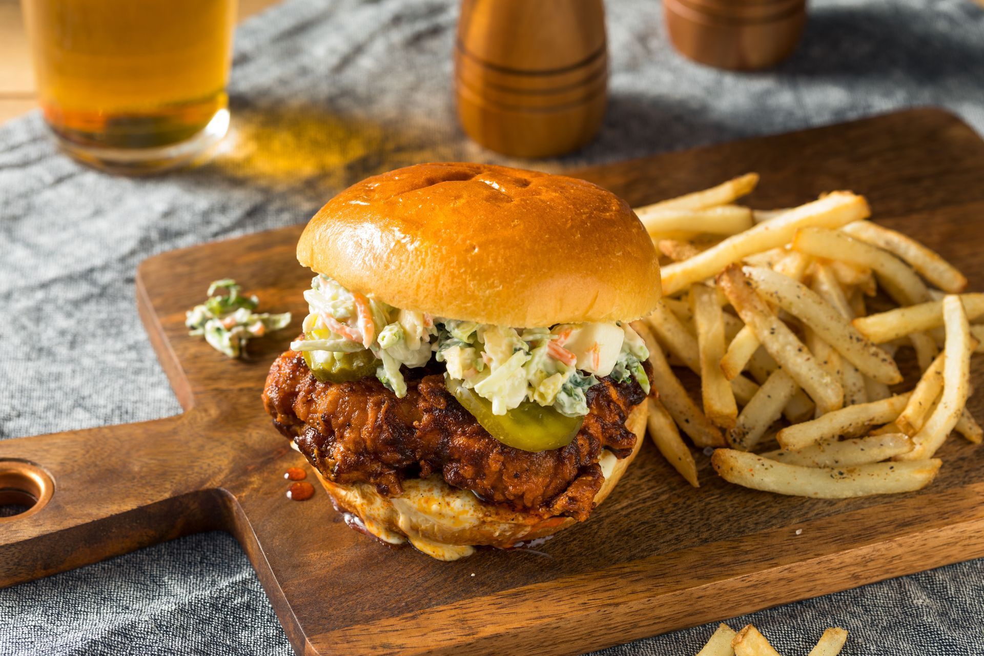 Fried chicken sandwich with fries and coleslaw on a wooden board.