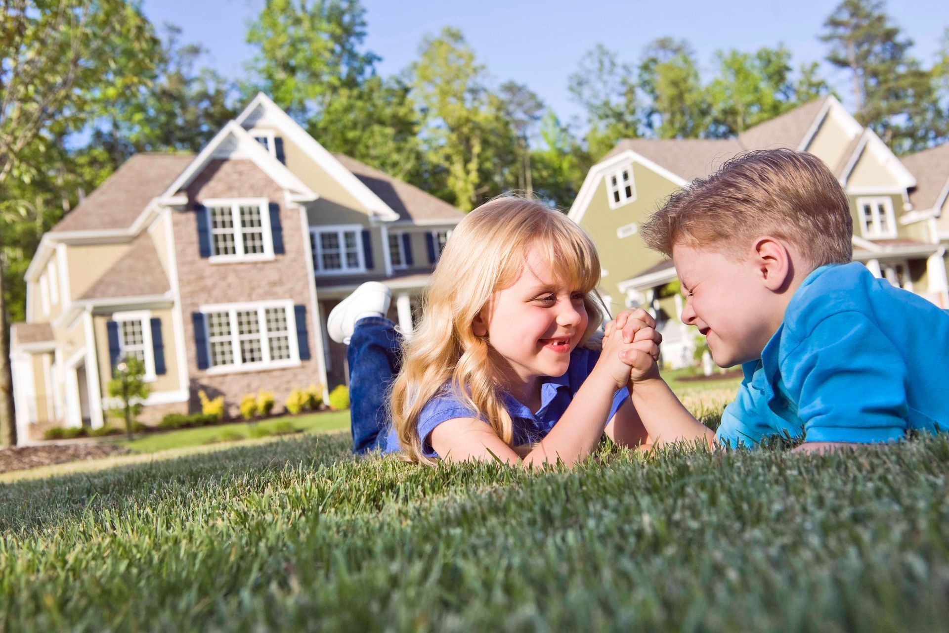Two children laughing on grass in front of houses.
