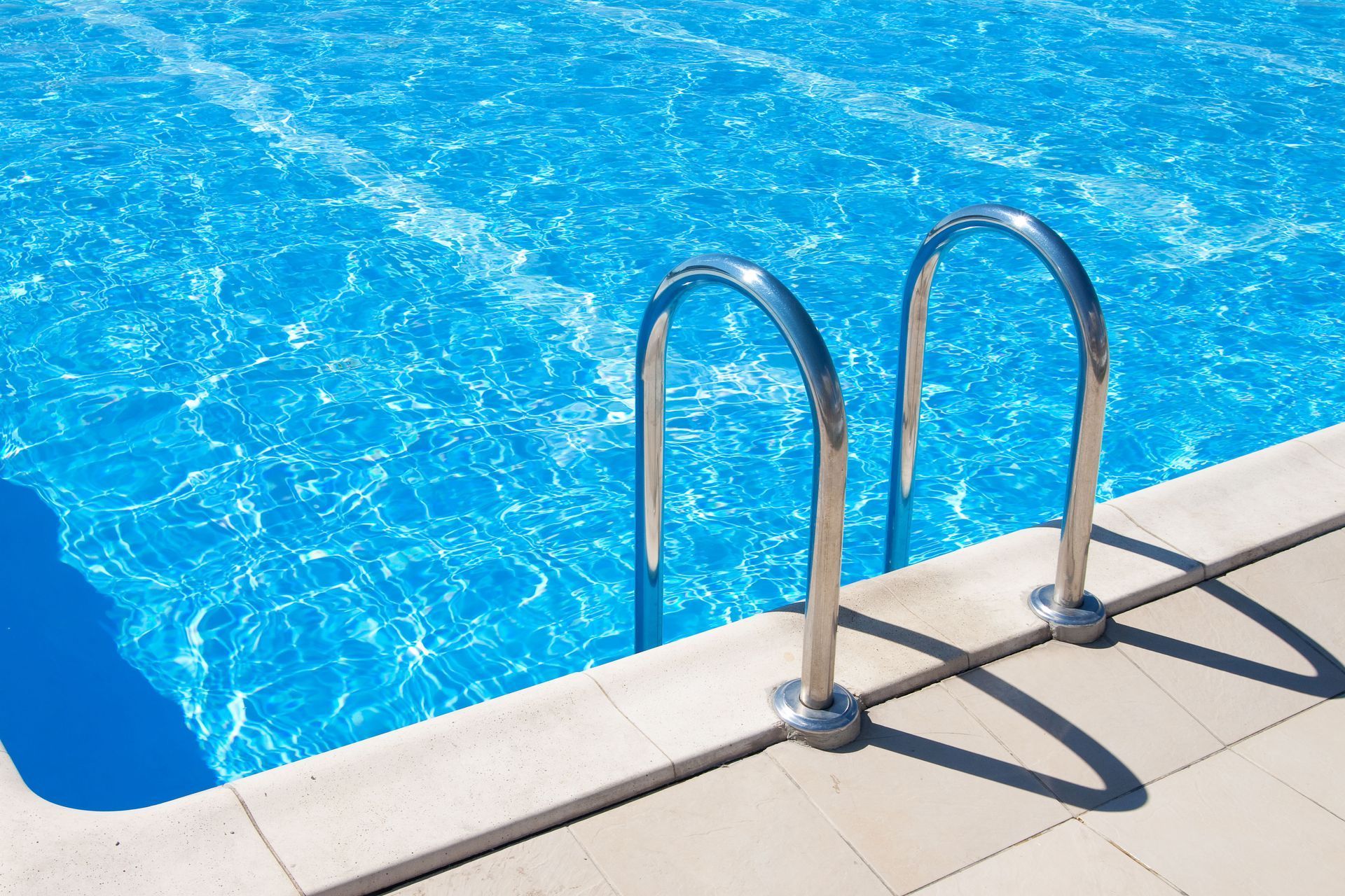 A swimming pool with clear blue water and chrome ladder. Sunny day.