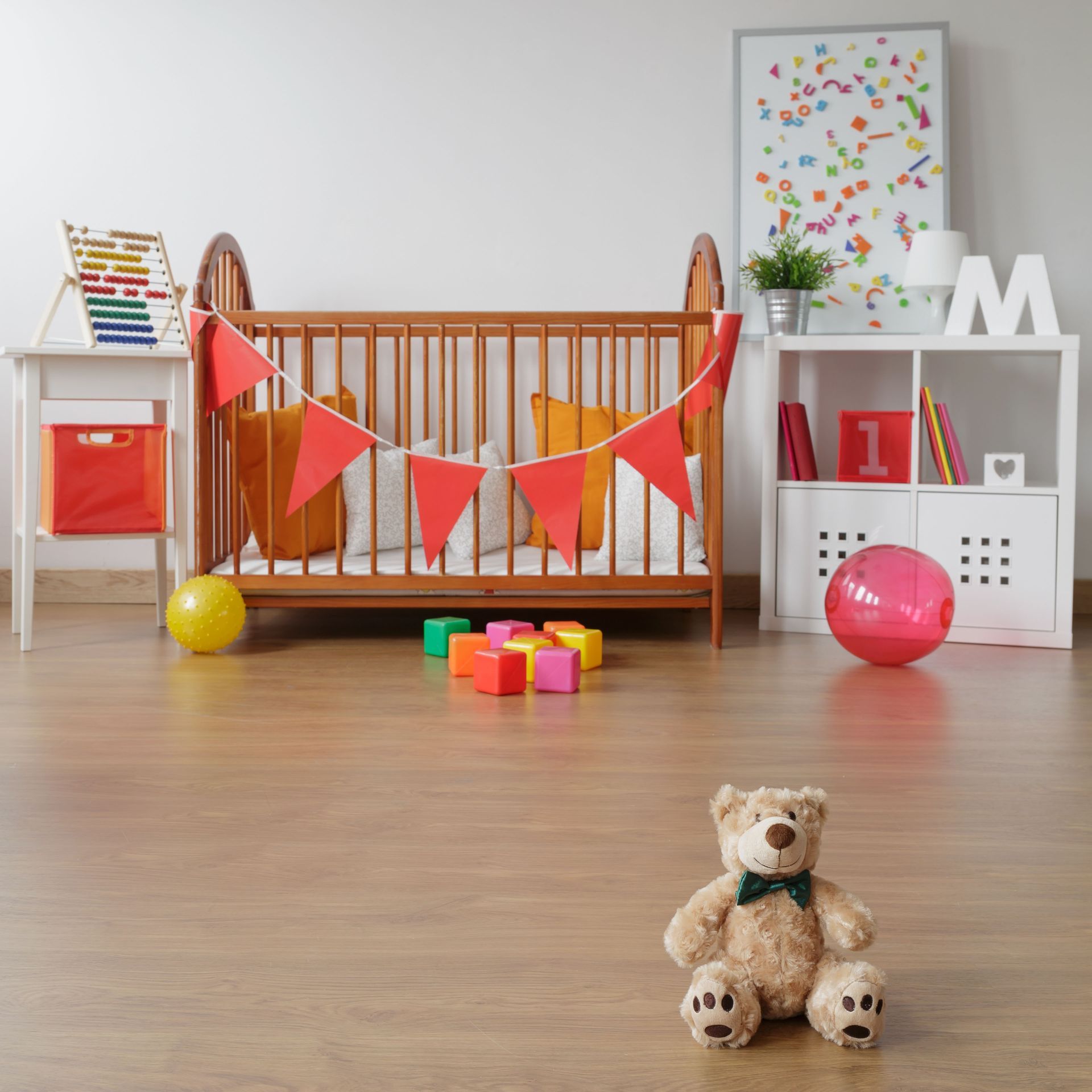 Cozy nursery with a wooden crib, colorful toys, and a teddy bear on the floor.