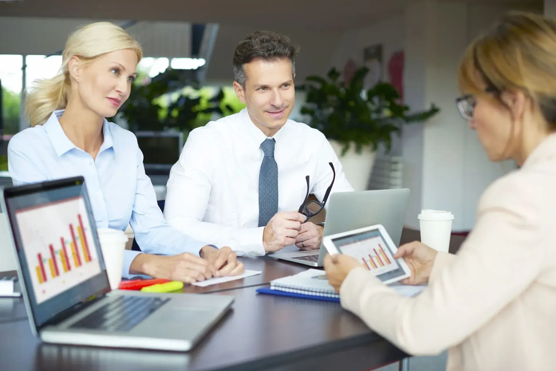 Business colleagues reviewing financial data. The woman in the foreground holds a tablet, others look on.