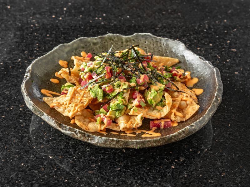 Chips topped with avocado, tuna, and seaweed, with a drizzle of sauce.