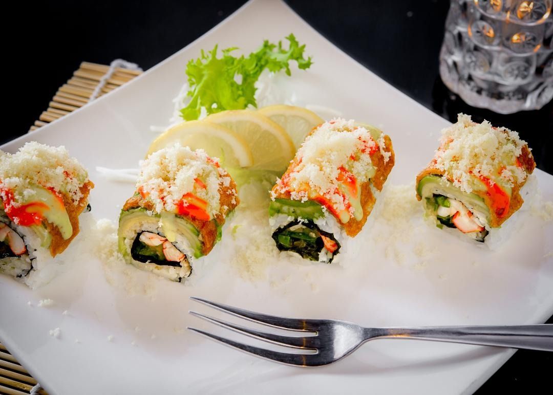Sushi rolls on a white plate, topped with grated cheese and avocado slices, served with a fork.