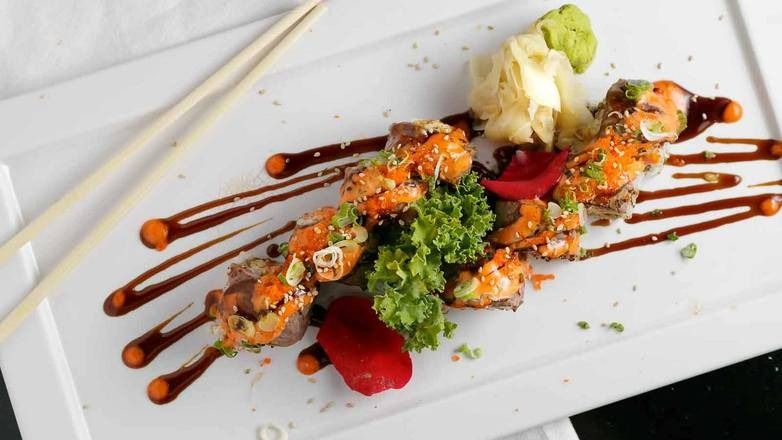 Sushi roll with shrimp, sauces, ginger, wasabi, and chopsticks on a white plate.