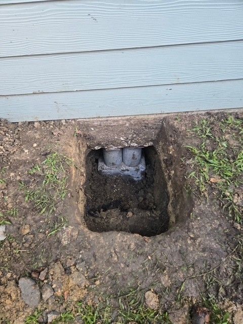 Hole dug near a house foundation, exposing pipes or supports set in concrete