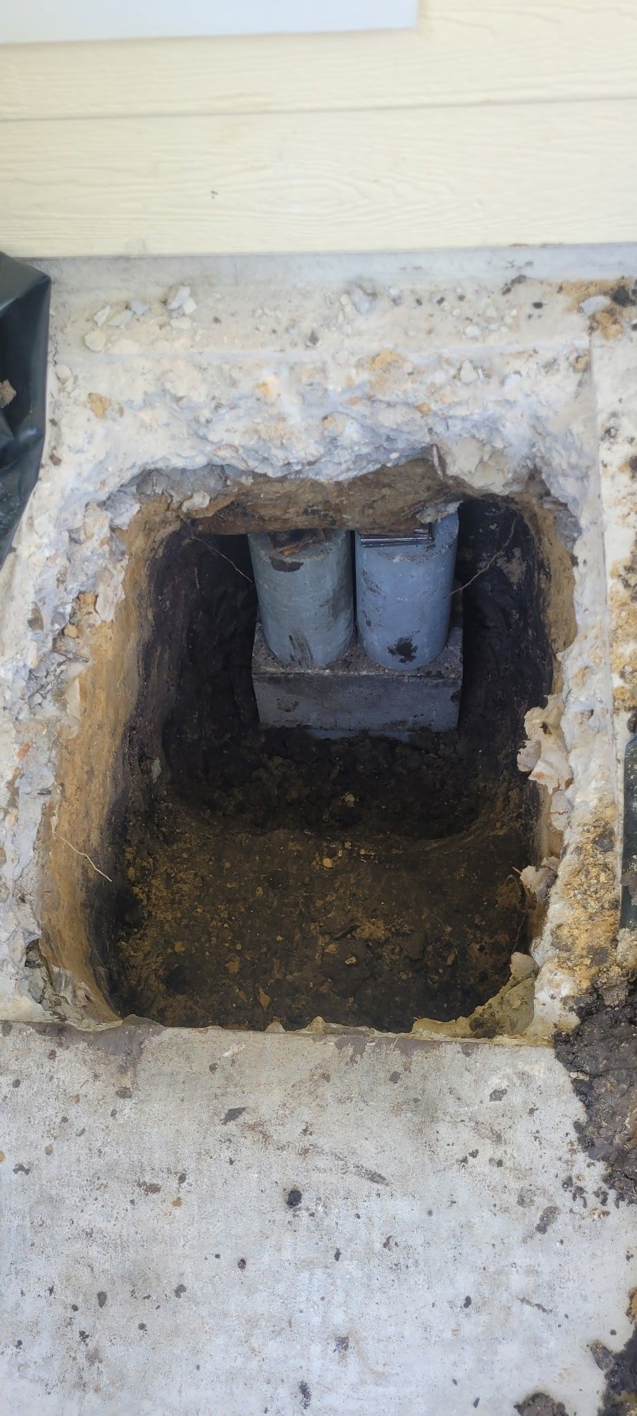 A rectangular hole in concrete reveals two pipes