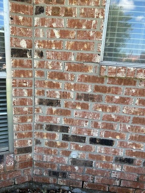 Brick exterior wall with window, vertical cracks, and some dark bricks
