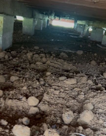Crawling space with soil, concrete pillars, and wood supports