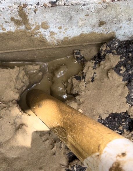 A white pipe expels muddy liquid onto a concrete surface