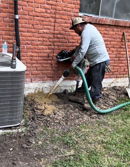 Man using a vacuum to dig near a brick building