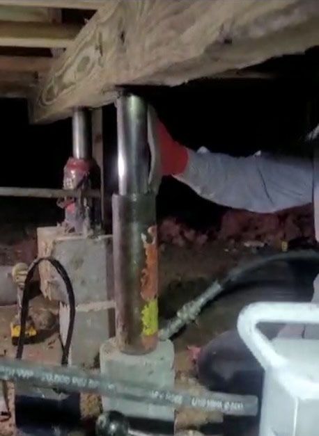 Worker uses a jack to lift a wooden beam under a house