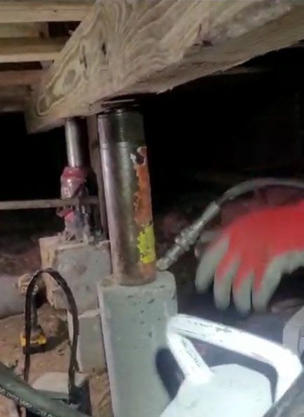 Hydraulic jacks supporting a wooden beam under a house