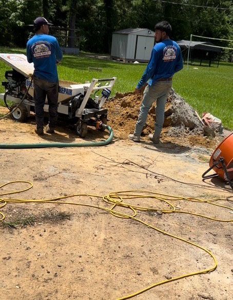 Two men in blue shirts operating machinery outdoors