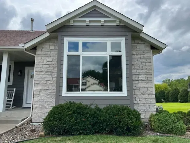 House exterior with bay window, light stone facade, gray siding, and green shrubs.