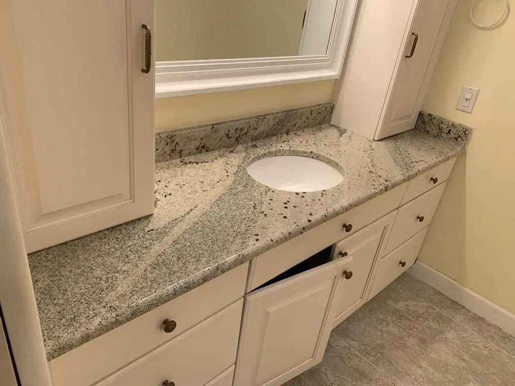 Bathroom vanity with granite countertop, round sink, mirror, and white cabinets