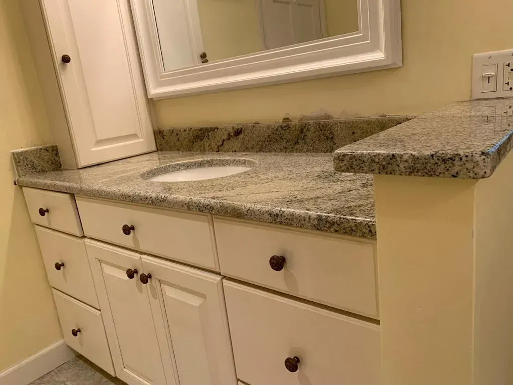 Granite bathroom vanity with double sinks, white cabinets, and a large framed mirror
