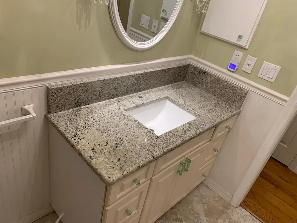 Bathroom vanity with speckled granite countertop, under-mount sink, mirror, and wood floor