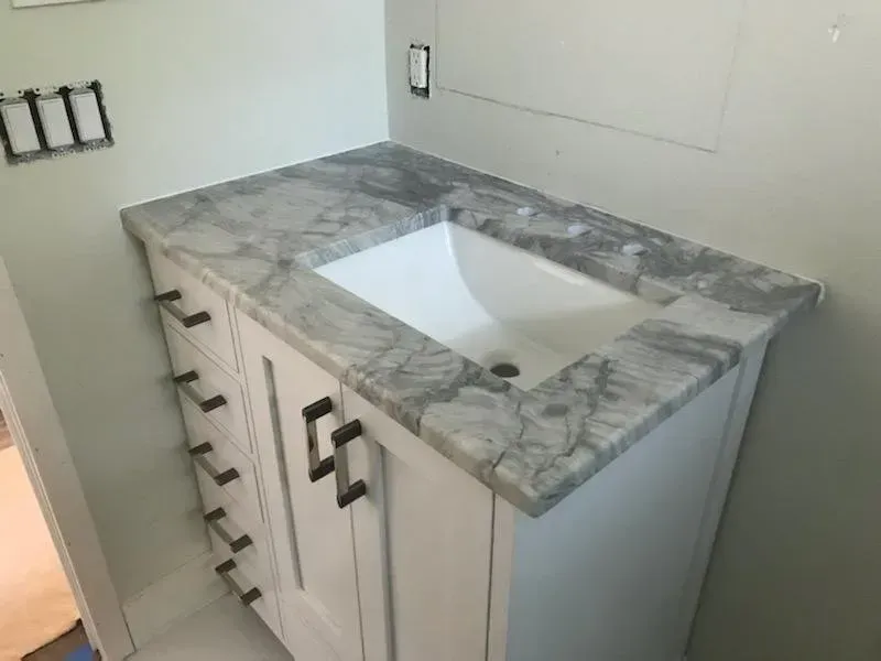 White bathroom vanity with gray marble countertop and rectangular sink in a tiled room