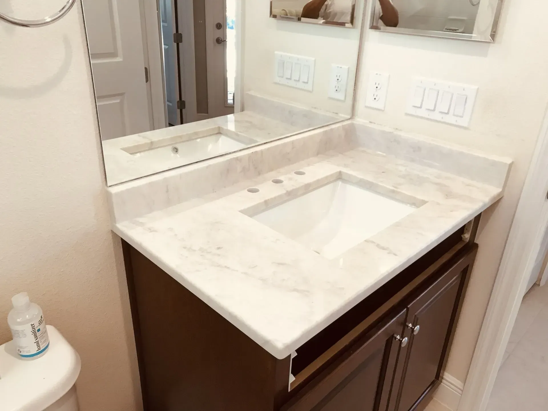 Bathroom vanity with white marble countertop, under-mount sink, and brown cabinets beneath a mirror.
